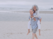 Older couple on beach with man giving woman a piggy back
